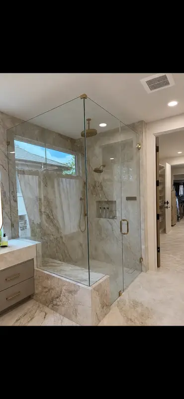 Frameless glass shower enclosure with brushed brass hardware and marble walls